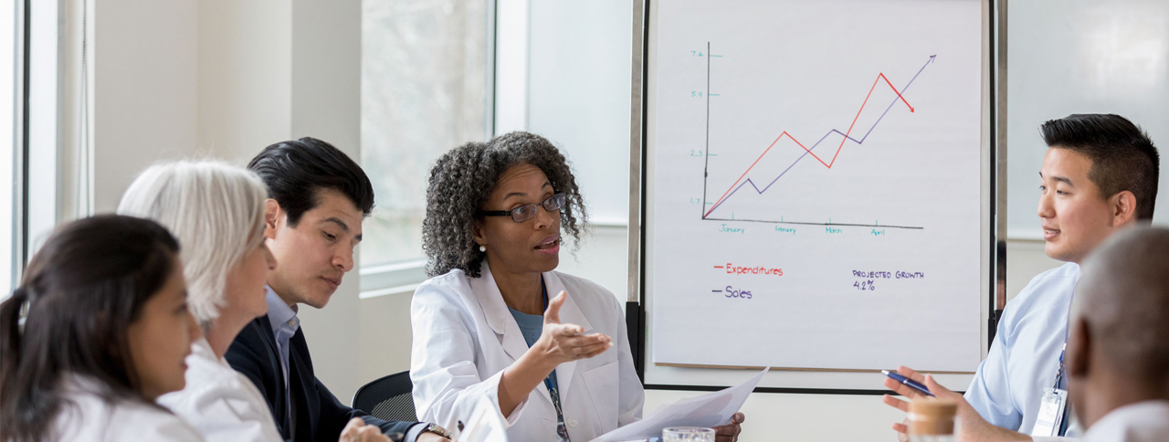 A woman in a lab coat explains a theory to peers.