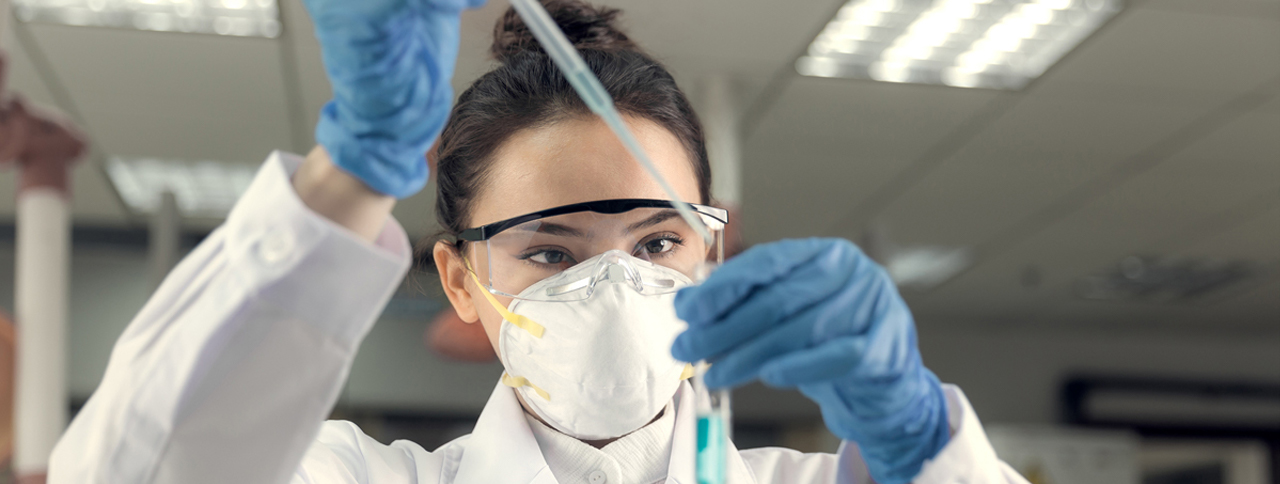 Female scientist looking at test tube and wearing mask